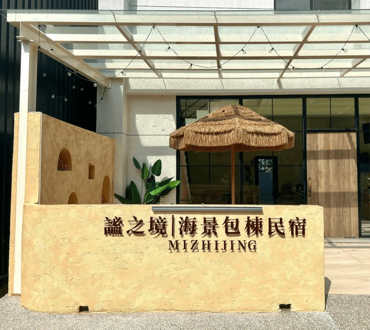 謐之境門口:土黃色矮牆上的店名招牌、草編陽傘與玻璃雨遮
